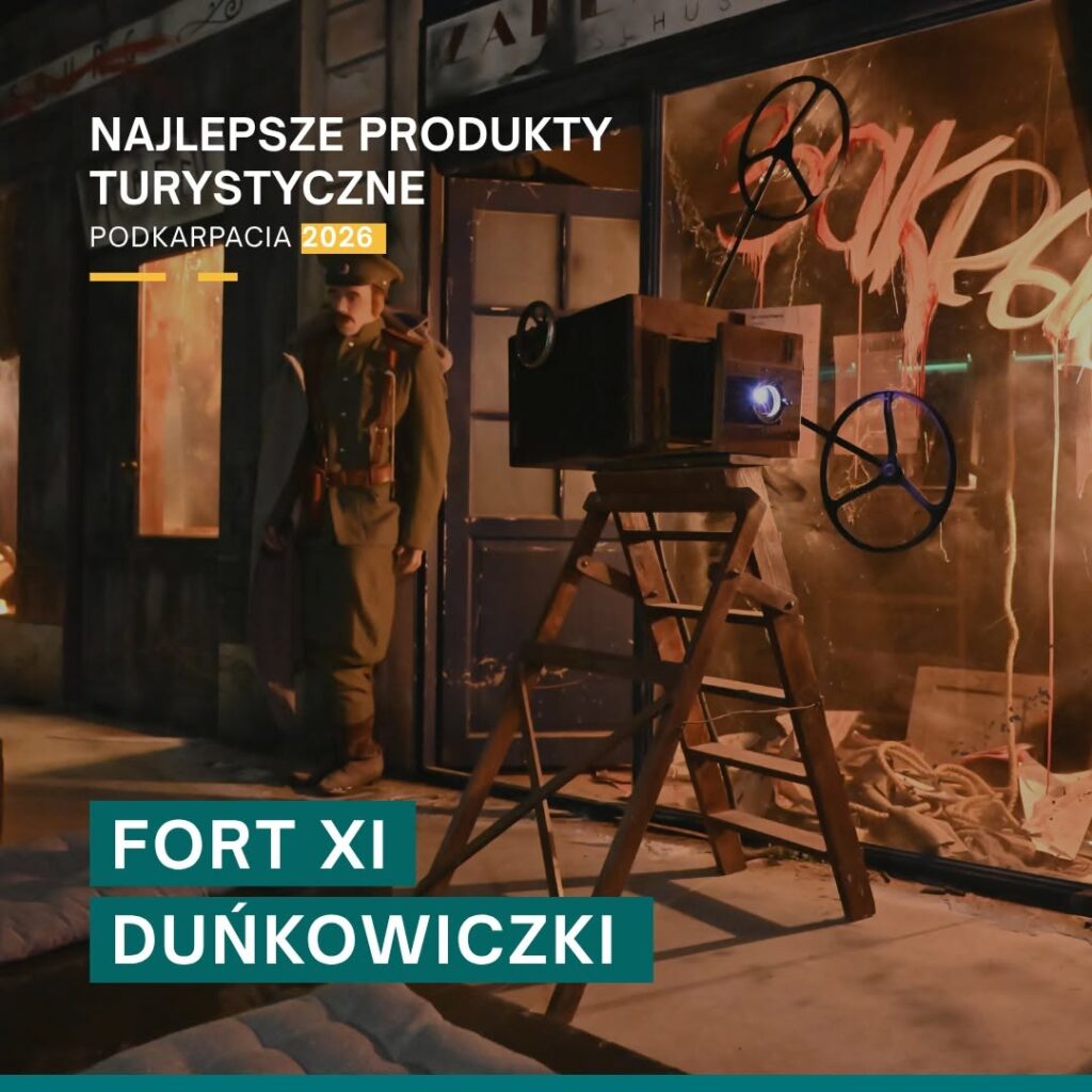 Sala ekspozycyjna wewnątrz fortu. Przedstawia zniszczone miasto po poddaniu się Twierdzy Przemyśl. Na pierwszym planie stoi kinematograf, obok żołnierz w mundurze rosyjskim. W tle poniszczone witryny sklepowe.

Na górze zdjęcia napis "Najlepsze produkty turystyczne Podkarpacia 2026. Na dole zdjęcia napis "Fort XI Duńkowiczki".